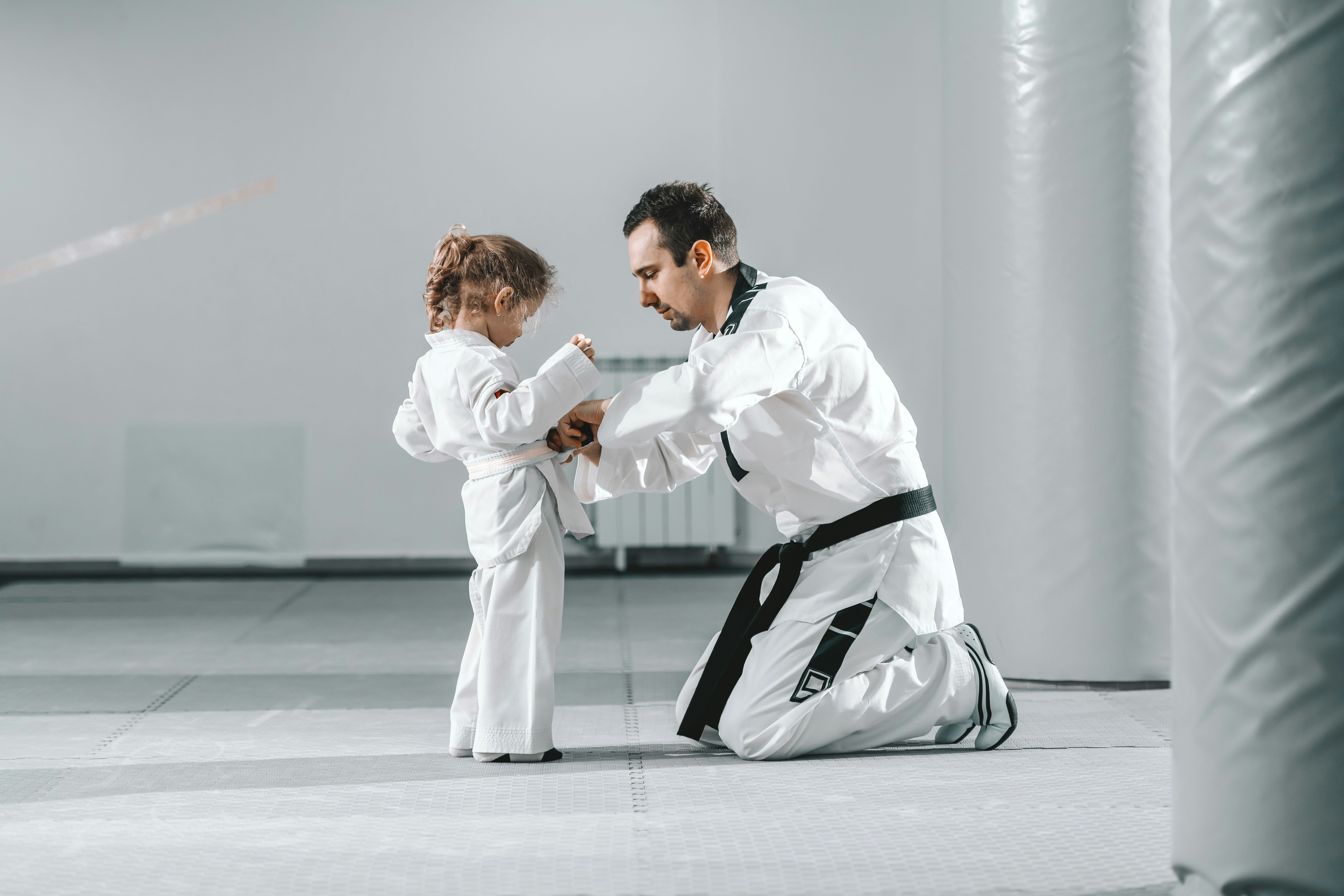 Teacher tying the belt of a kid student in her first martial arts class