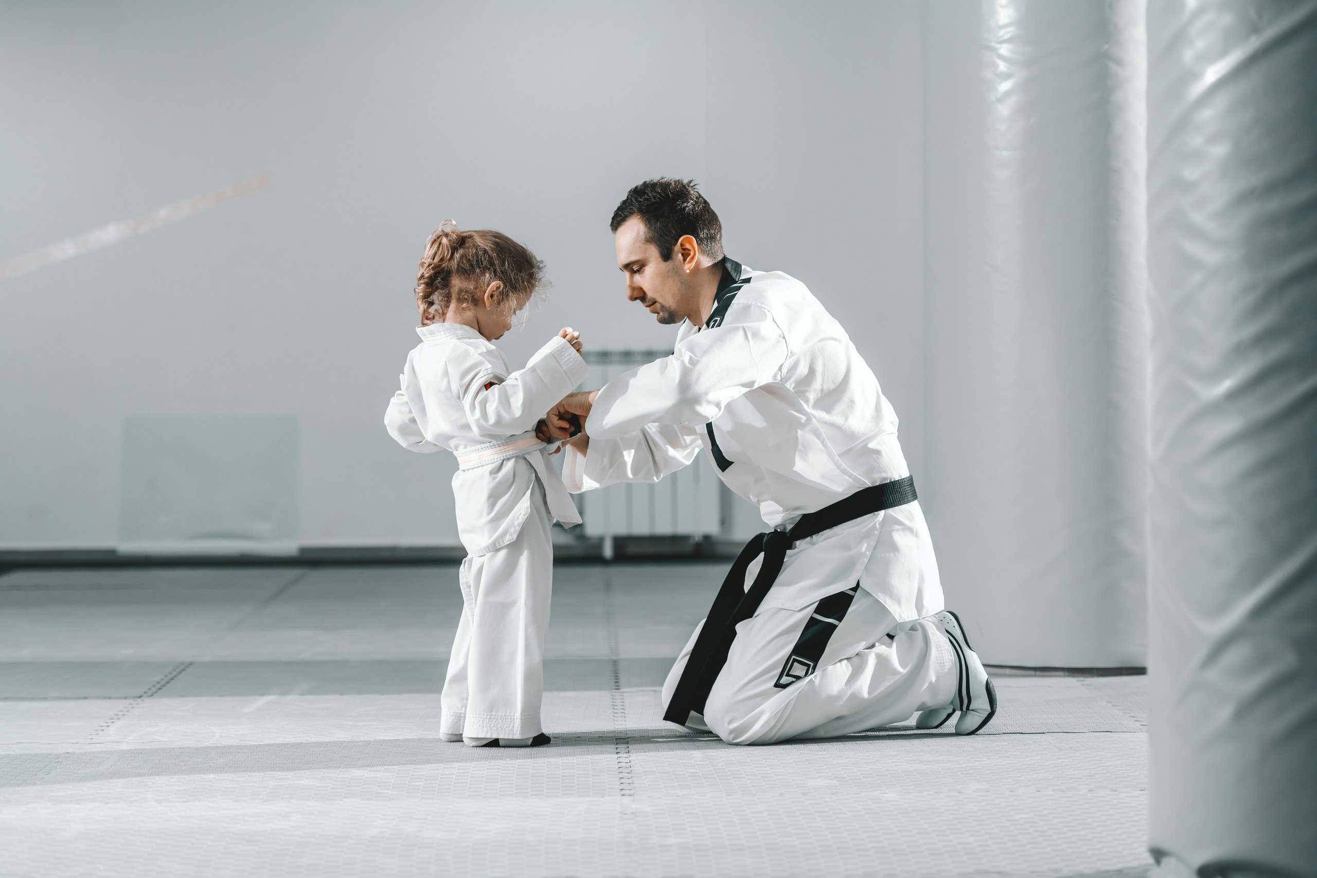 Teacher tying the belt of a kid student in her first martial arts class