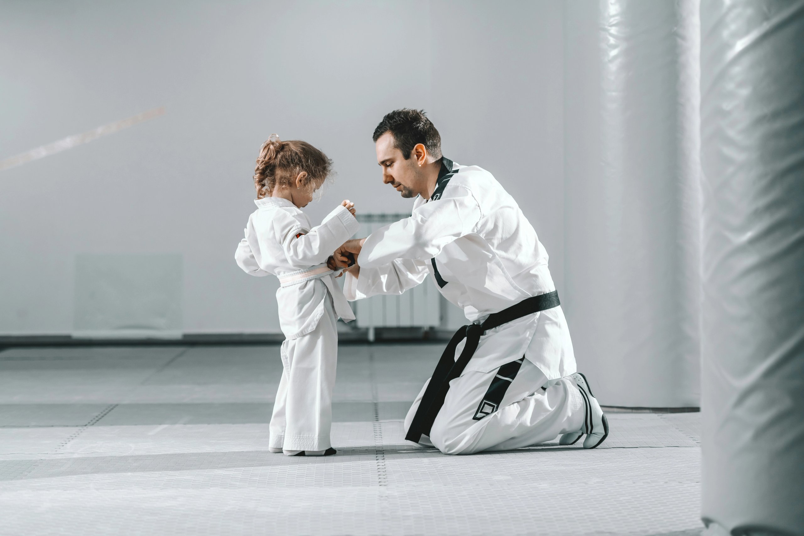 Teacher tying the belt of a kid student in her first martial arts class