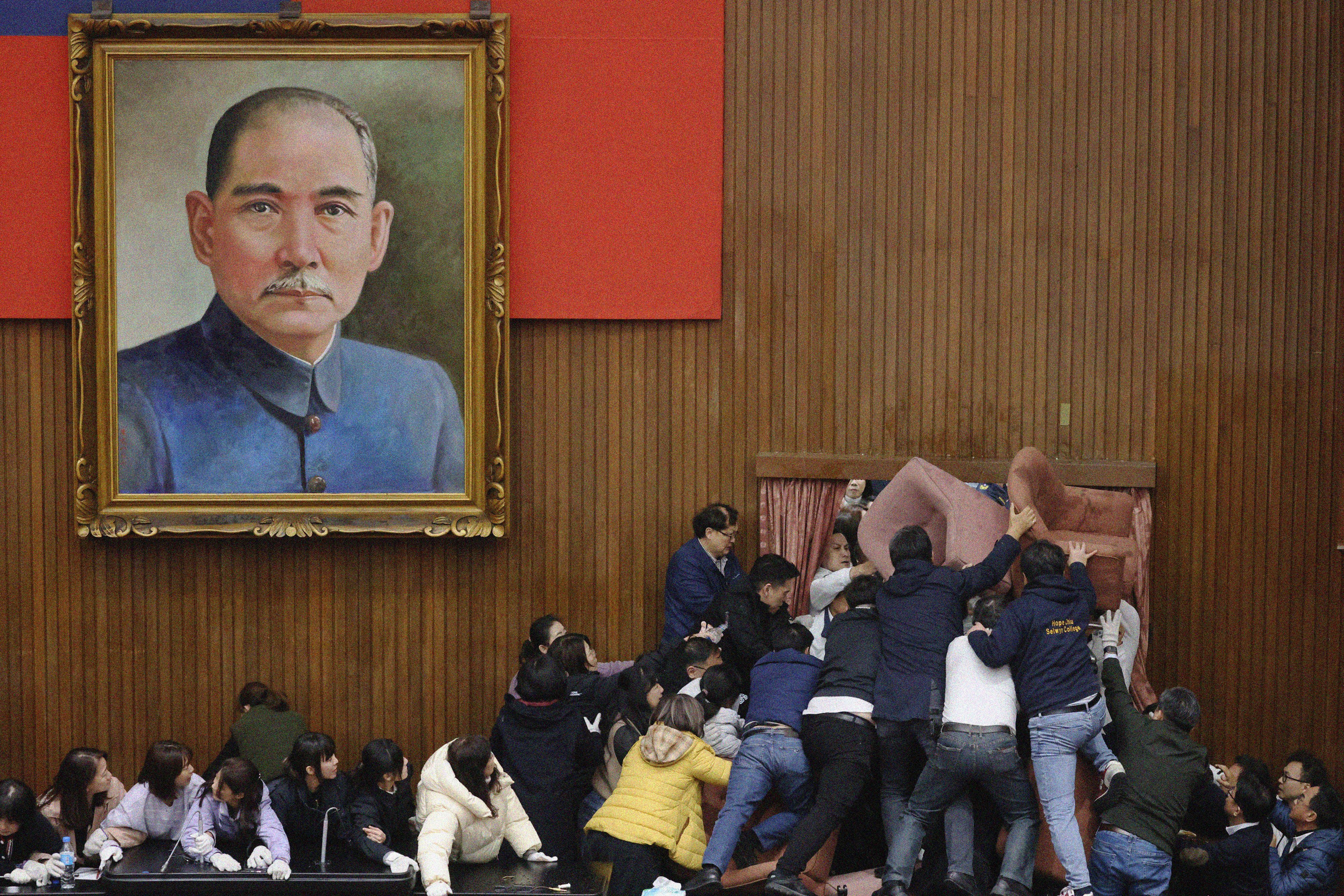 People crowd into a doorway in a parliament building, with a large portrait next to the door.