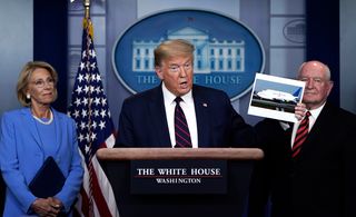 President Donald Trump holds up a picture of a Boeing 747 Dreamlifter during a briefing on the coronavirus pandemic briefing