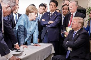 Angela Merkel and other world leaders stand around a seated Donald Trump