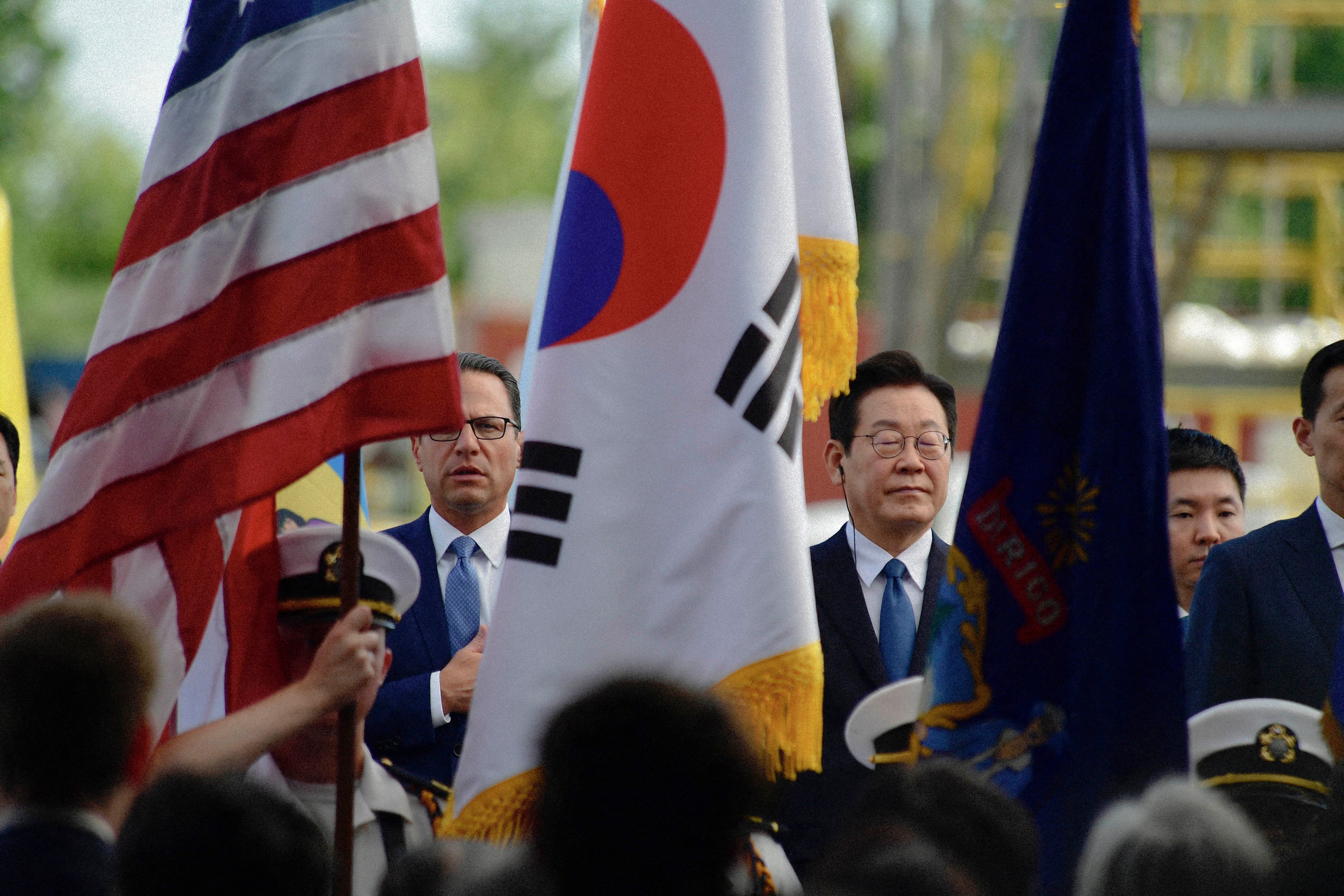 Two people standing in crowd with USA and Korean flags in front of them.