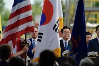 Two people standing in crowd with USA and Korean flags in front of them.