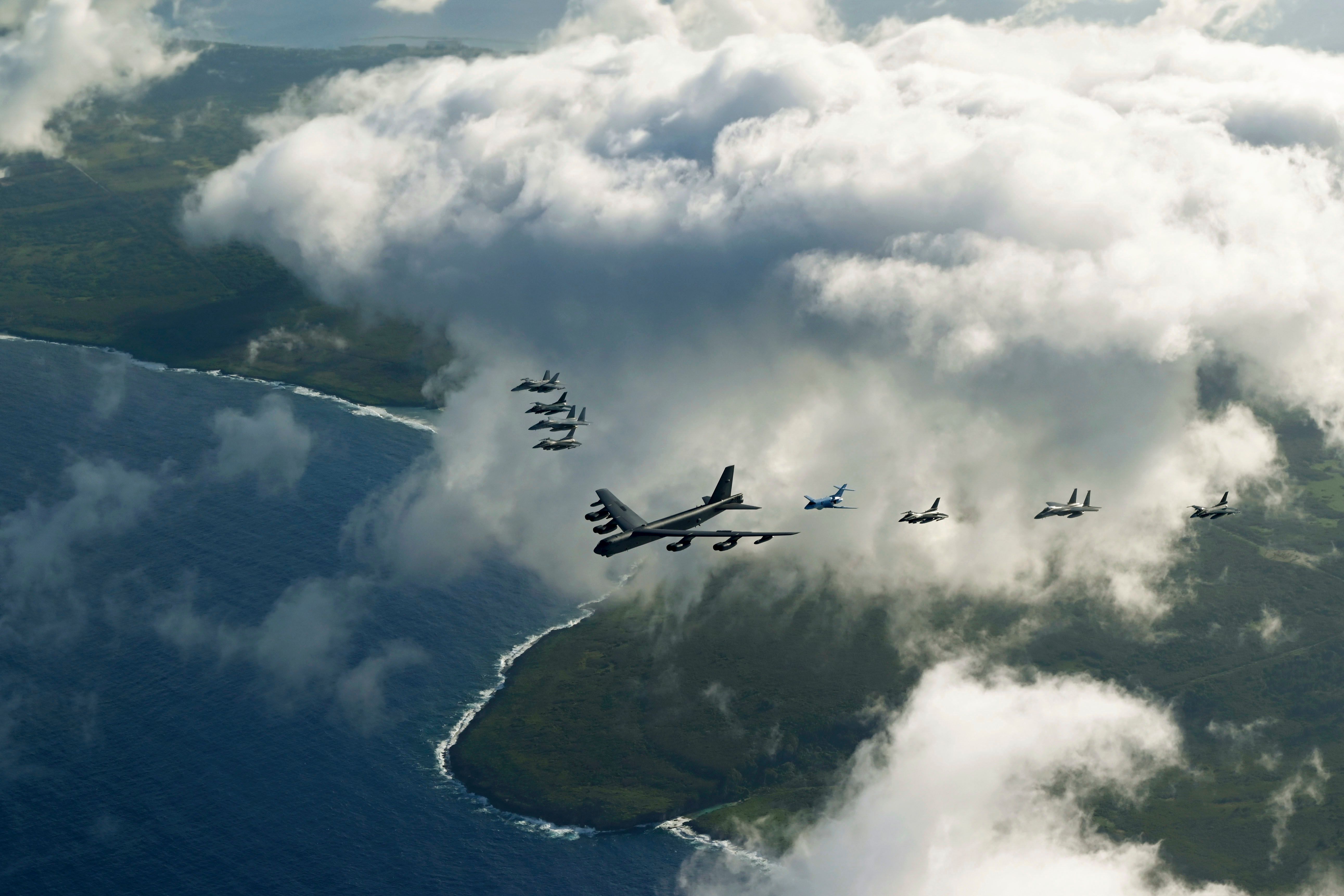 US and Japanese military aircraft flying in formation above ocean and coastline.