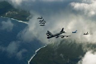 US and Japanese military aircraft flying in formation above ocean and coastline.