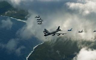 US and Japanese military aircraft flying in formation above ocean and coastline.