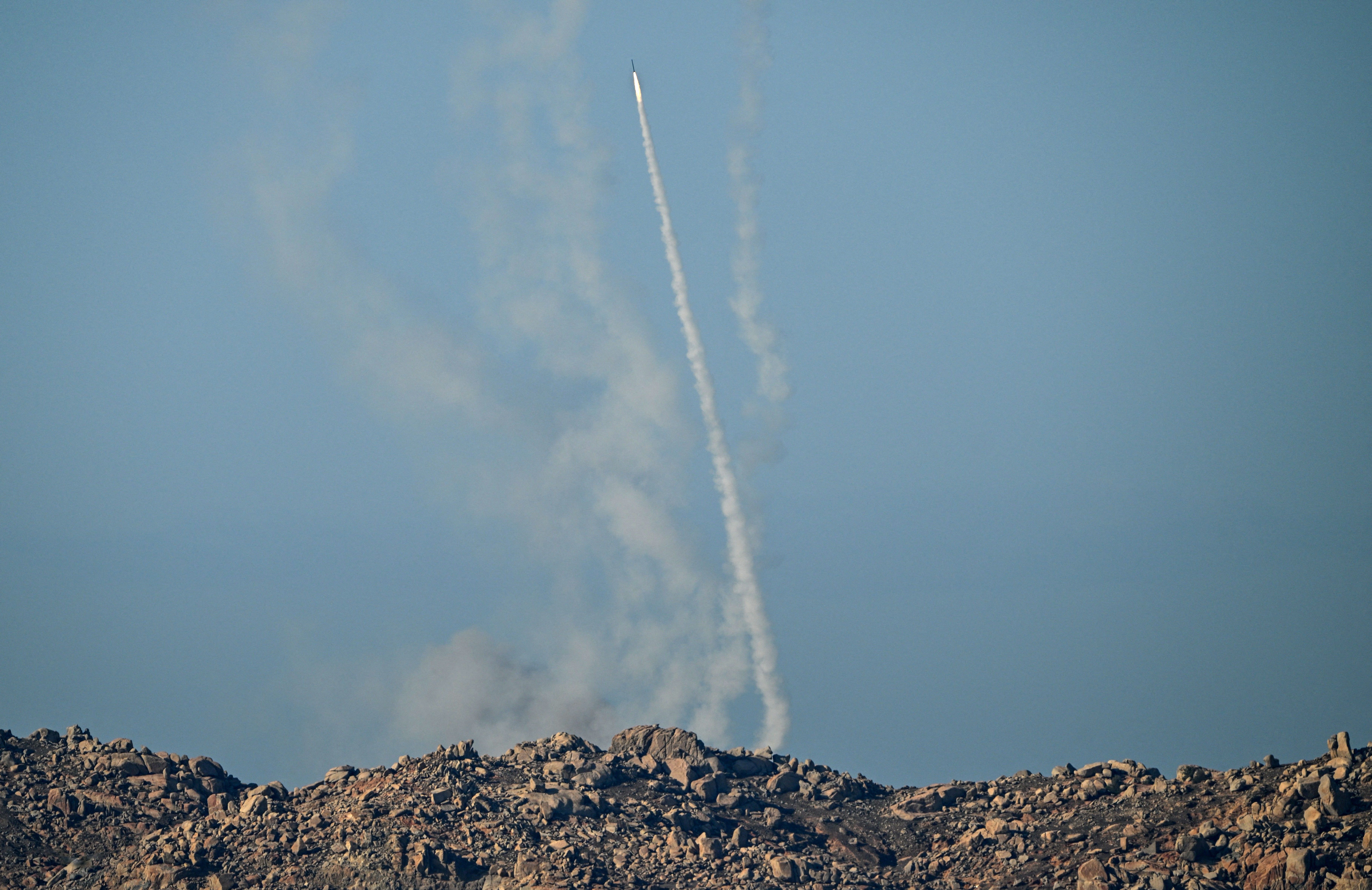 A missile taking off into the sky with rocky terrain in the foreground.