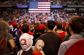 A woman wearing a QAnon hat with her baby listen to President Trump speak at the Mohegan Sun Arena, Pennsylvania, August 2018
