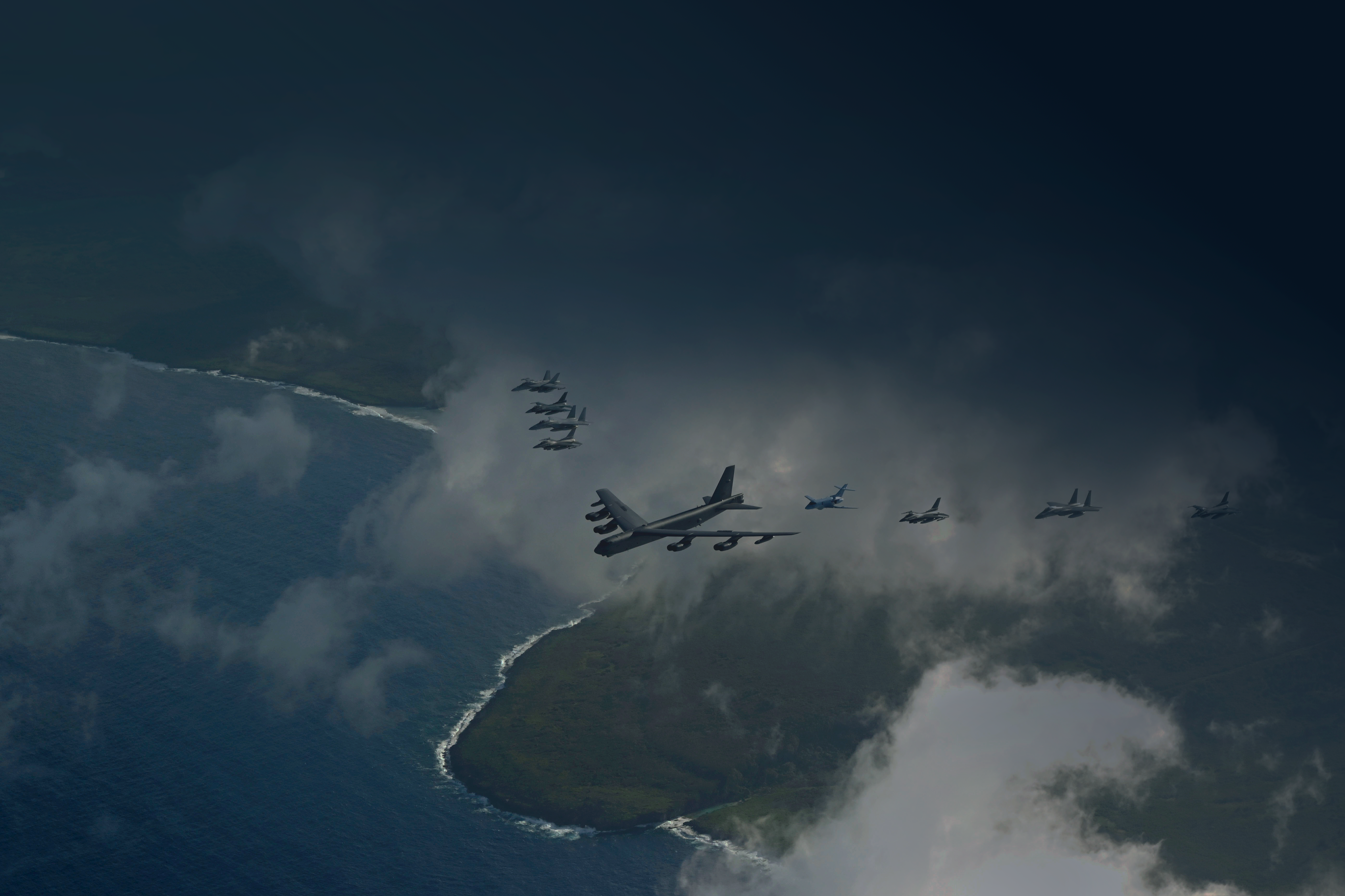US and Japanese military aircraft flying in formation above ocean and coastline.