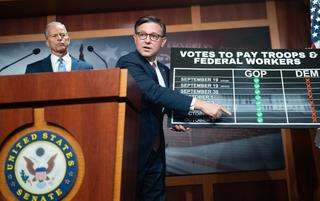 Speaker of the House Mike Johnson holds up a chart about paying the military and federal workers during a news conference with Senate Majority Leader John Thune, October 2025