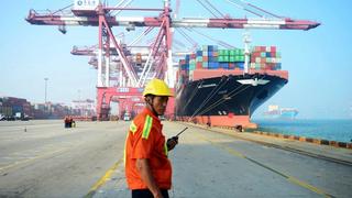 A Chinese worker looks on as a cargo ship is loaded at a port in Qingdao, China