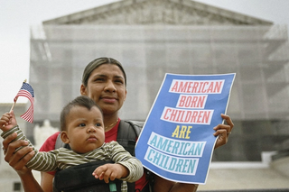 Woman with child standing out the front of the US Supreme Court building holding a sign