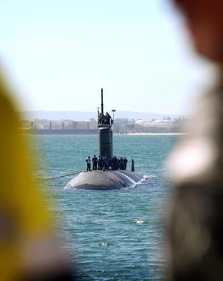 Submarine coming into port, with sailors standing on top.