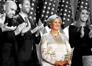 Susie Wiles looks on, on a stage with a group of people as Donald Trump makes his election victory speech.