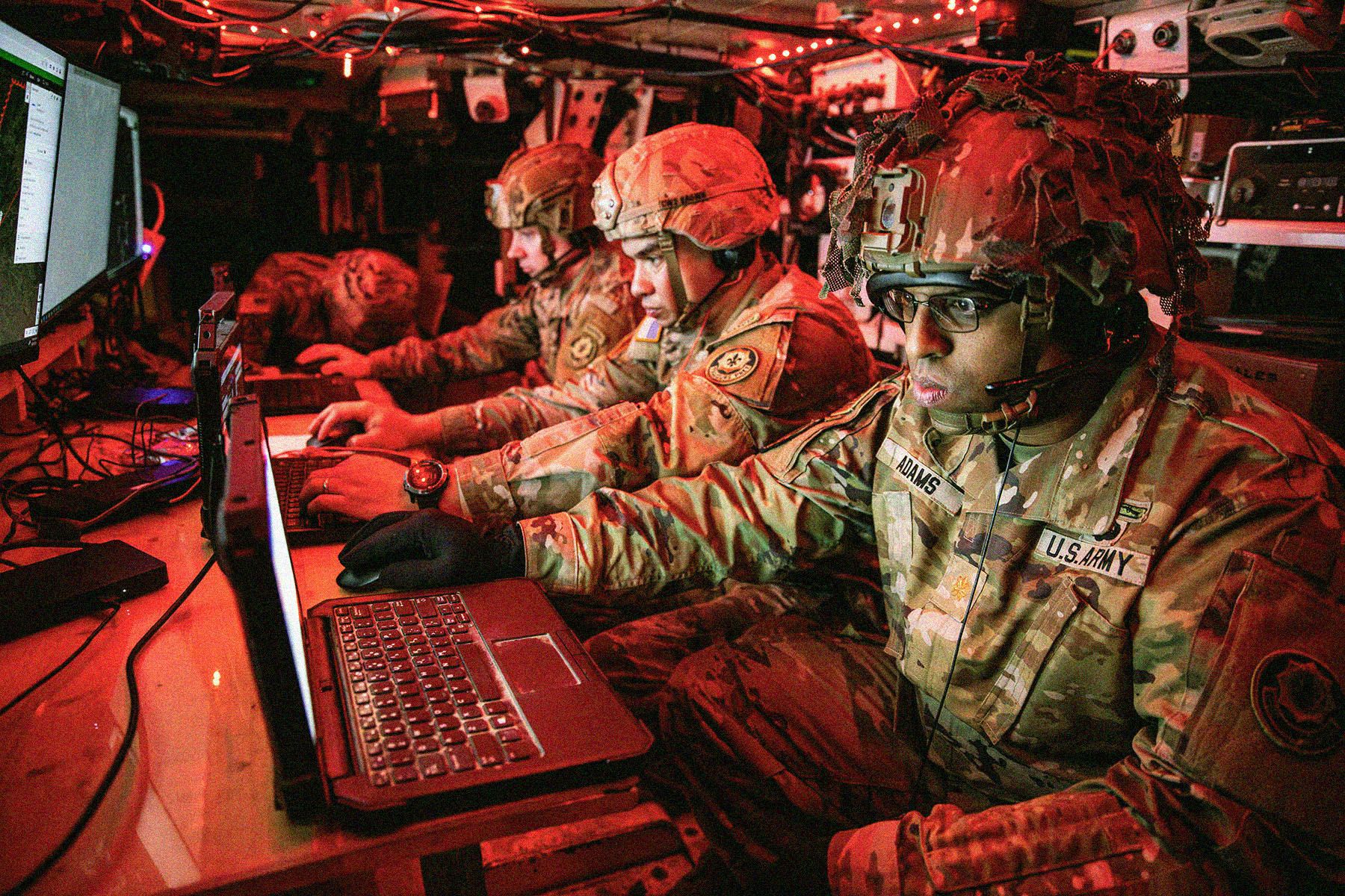 Three soldiers in uniform, working on laptop devices inside an armoured vehicle.