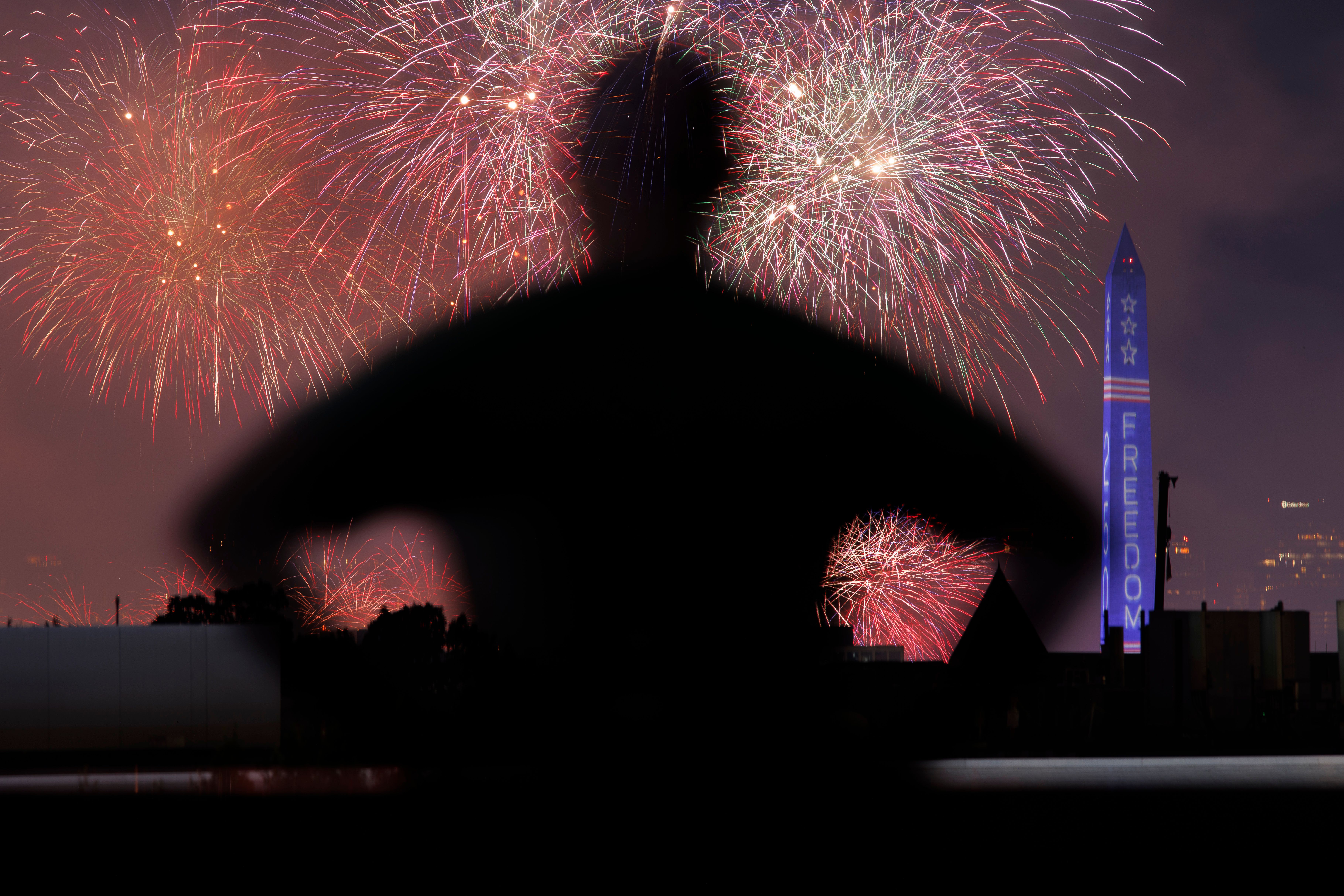 A person watches fireworks from the Freedom 250  Salute to America Independence Day celebration go off behind the Washington Monument during a thunderstorm on July 5, 2026 in Washington, DC.