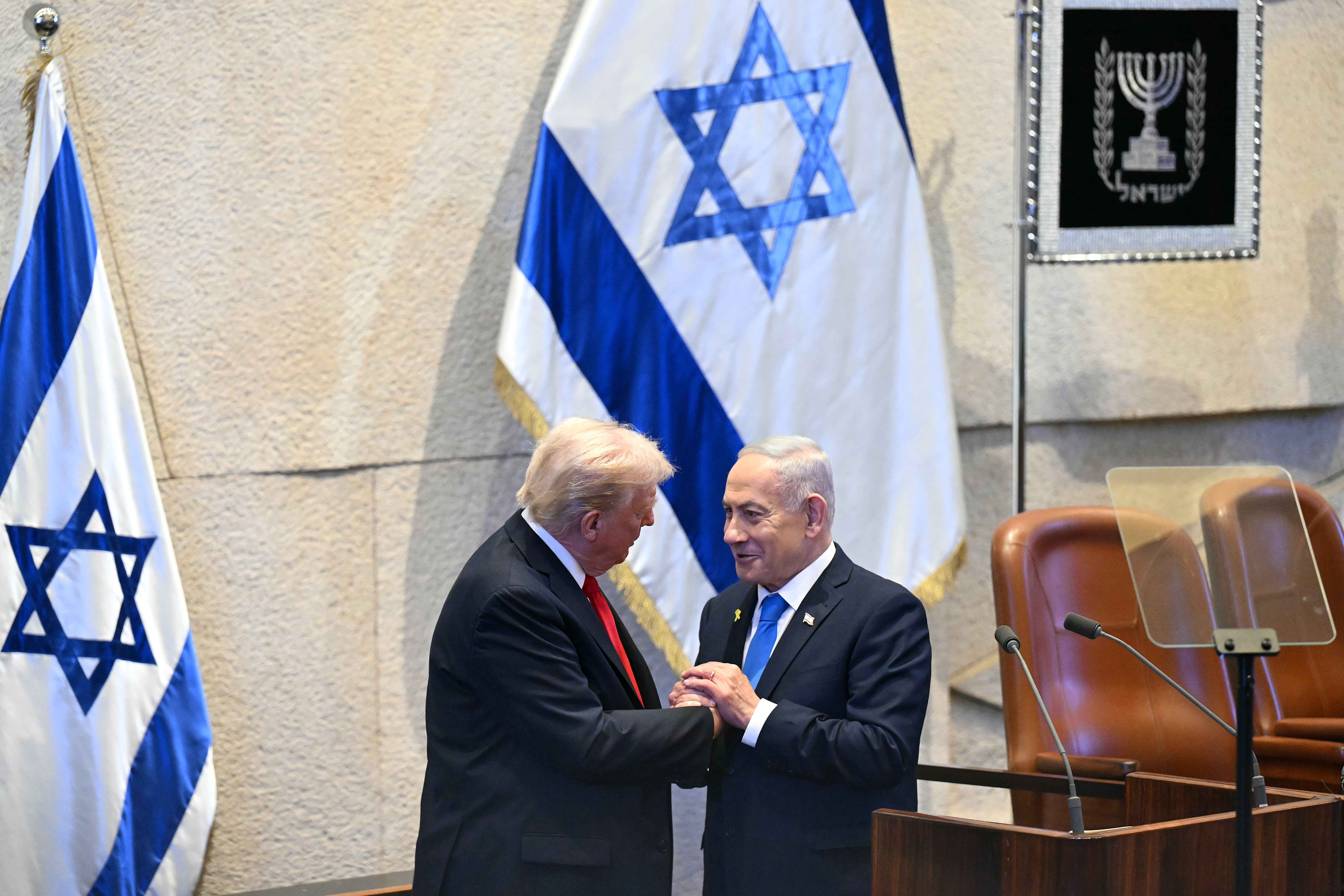 U.S. President Donald Trump (L) holds hands and speaks with Israeli Prime Minister Benjamin Netanyahu at the Israeli parliament, the Knesset, on October 13, 2025 in Jerusalem. President Trump is visiting the country hours after Hamas released the remaining Israeli hostages captured on Oct. 7, 2023, part of a US-brokered ceasefire deal to end the war in Gaza. 