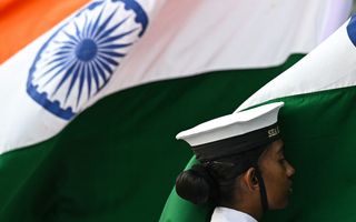 A sea cadet of the Indian Navy stands beside the country’s national flag during Navy Day celebrations at the Gateway of India in Mumbai, December 2023