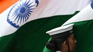 A sea cadet of the Indian Navy stands beside the country’s national flag during Navy Day celebrations at the Gateway of India in Mumbai, December 2023