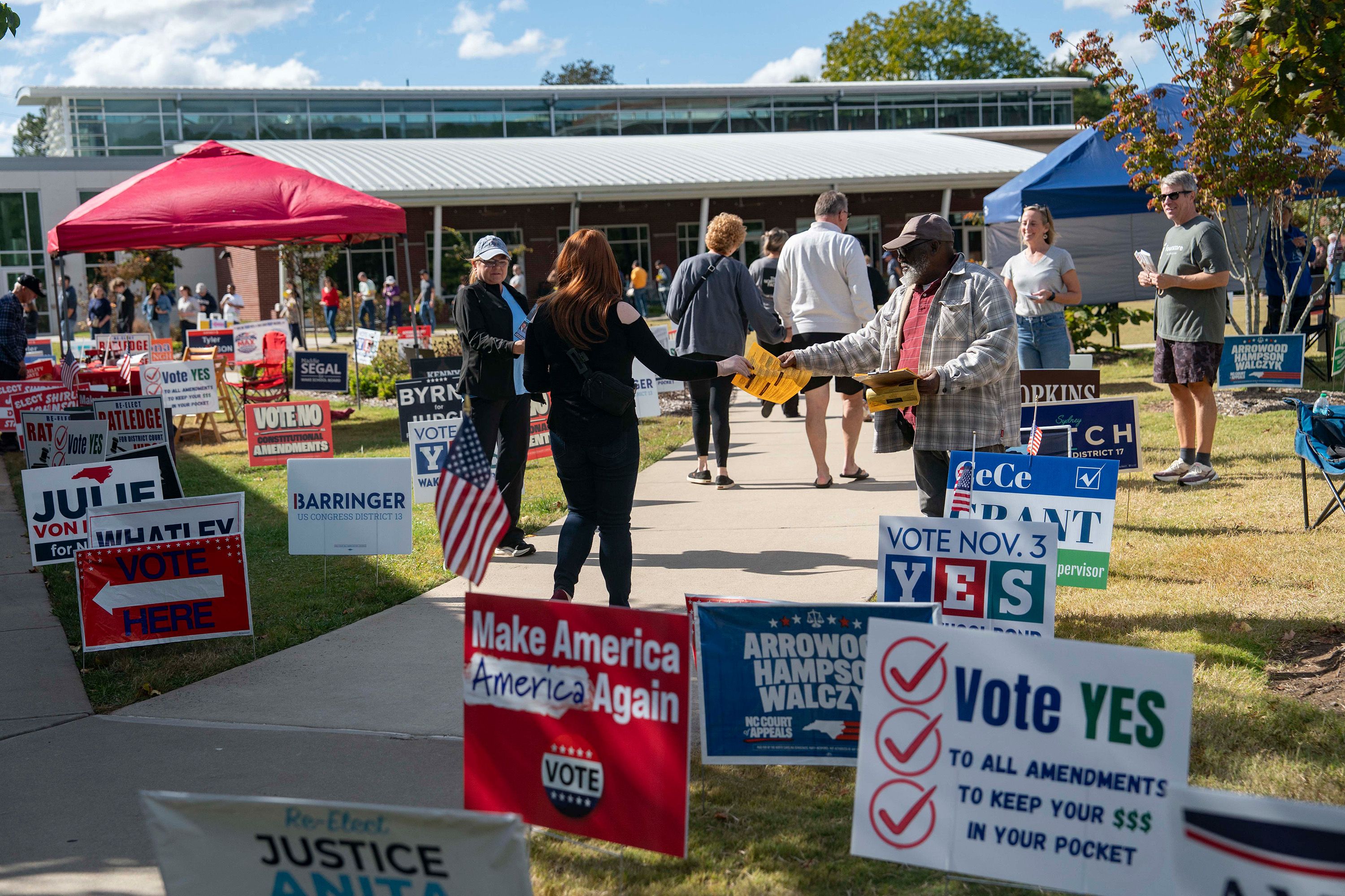 People walk past campaign signs as they go to participate in early voting for the midterm elections on October 25, 2026 in Cary, North Carolina.