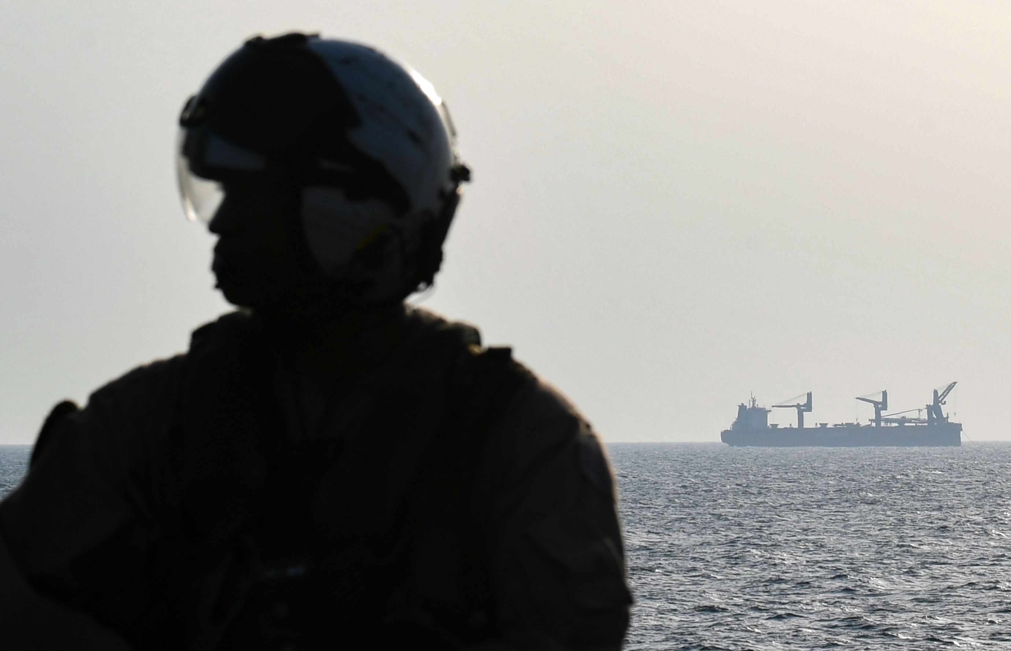 A commercial vessel is seen in the background as a US Black Hawk helicopter crew member stands on the deck of Britain's RFA Cardigan Bay landing ship in the Gulf waters off Bahrain during the International Maritime Exercise (IMX), on November 5, 2019. - IMX is a joint military exercise involving assets and personnel from more than 50 partner nations and seven international organisations. The US has pushed for the creation of a US-led operation dubbed the International Maritime Security Construct to safeguard trade and the flow of oil through the Strait of Hormuz. It has so far been joined by Australia, Britain and the United Arab Emirates, as well as Bahrain, the Gulf island state which is home to the US Fifth Fleet. 