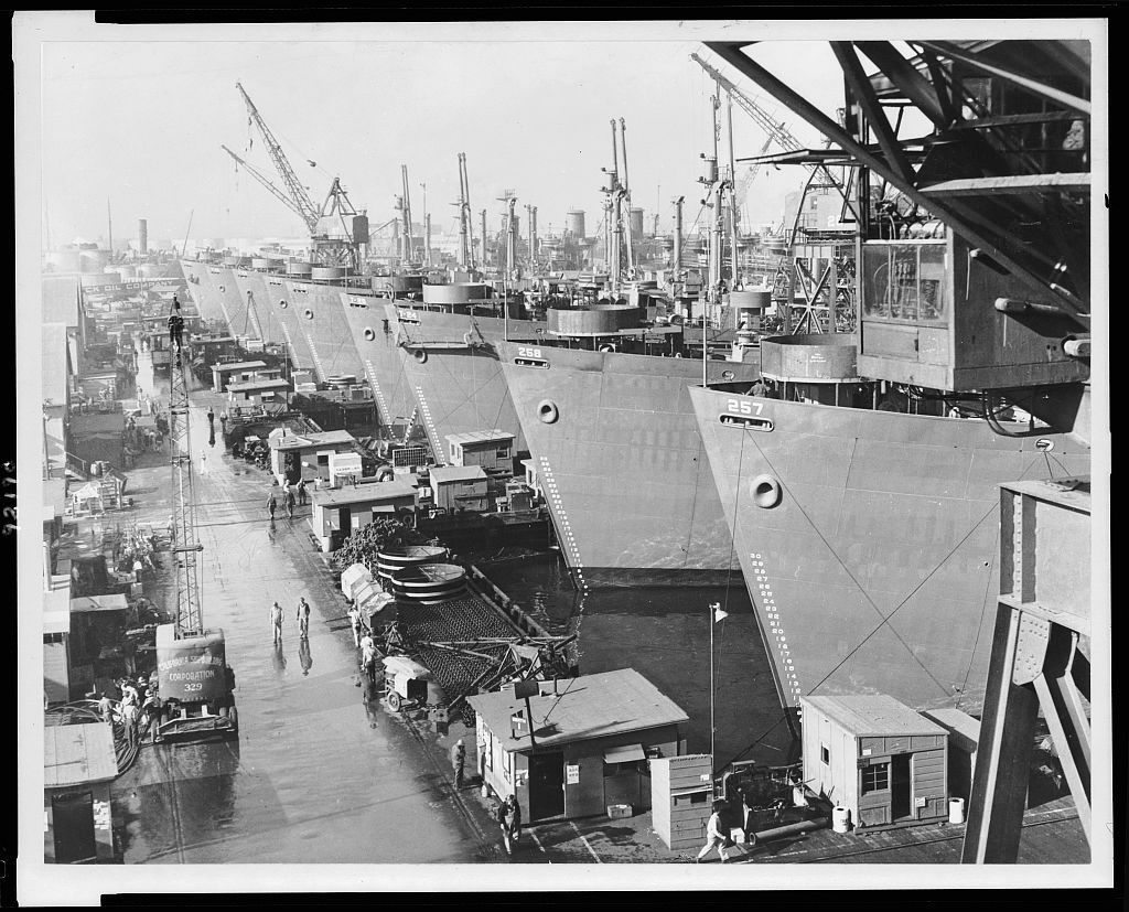 A line of ships at a shipyard facility, in black and white.