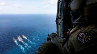 An aircrewman watches out of HMAS Arunta’s MH-60R helicopter ‘Athena’ as HMAS Arunta and USS Milius conduct a dual replenishment at sea with JS Oumi during Exercise Malabar 2022