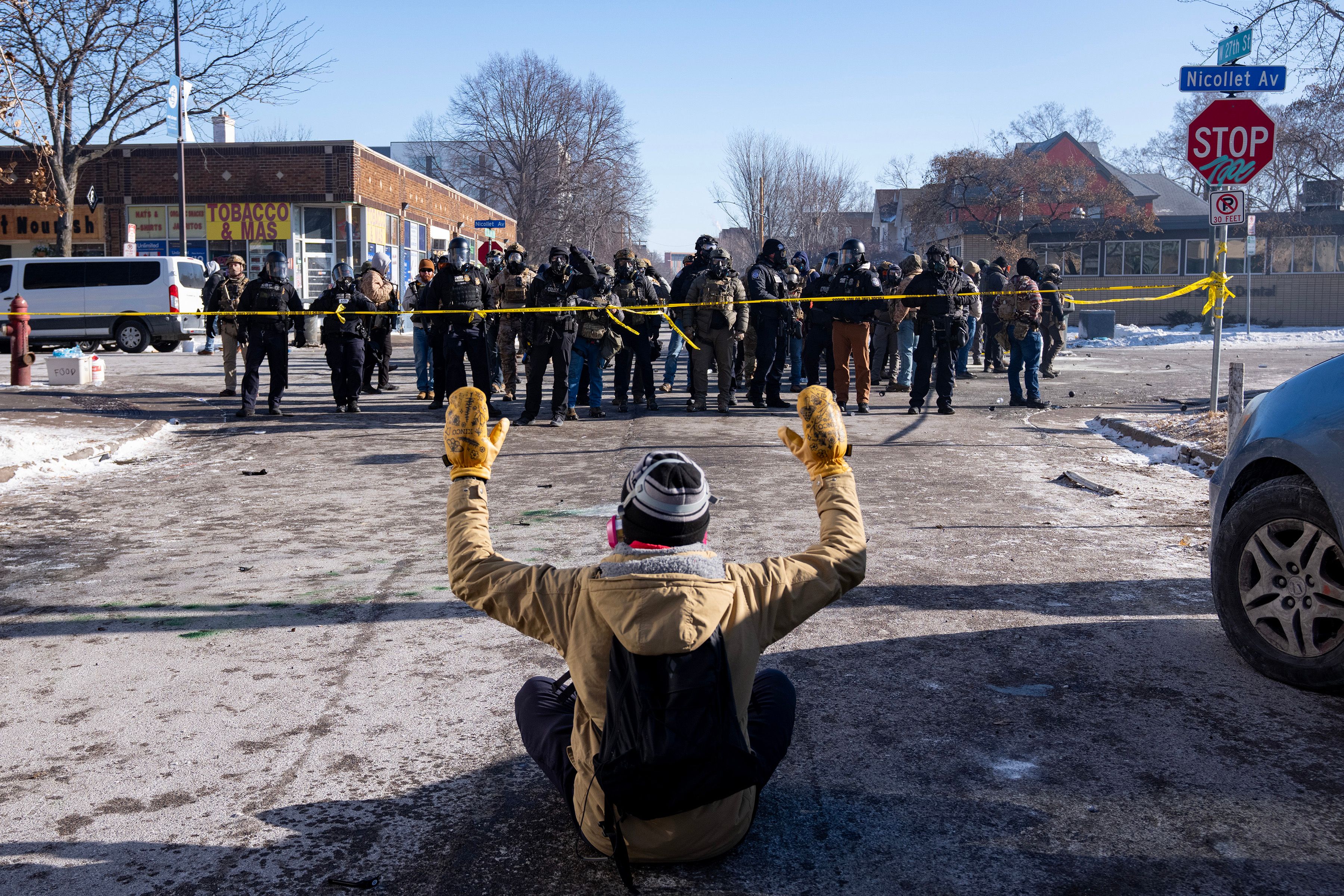 A protester sits on the street with his arms up in front of federal agents and police in south Minneapolis after Alex Pretti was fatally shot by federal agents in the area early Saturday morning, 24 January 2026