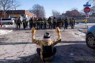 A protester sits on the street with his arms up in front of federal agents and police in south Minneapolis after Alex Pretti was fatally shot by federal agents in the area early Saturday morning, 24 January 2026