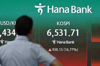 A man stands near an electronic screen showing South Korea's benchmark stock index (KOSPI) in a foreign exchange dealing room at the Hana Bank headquarters in Seoul on July 31, 2026.
