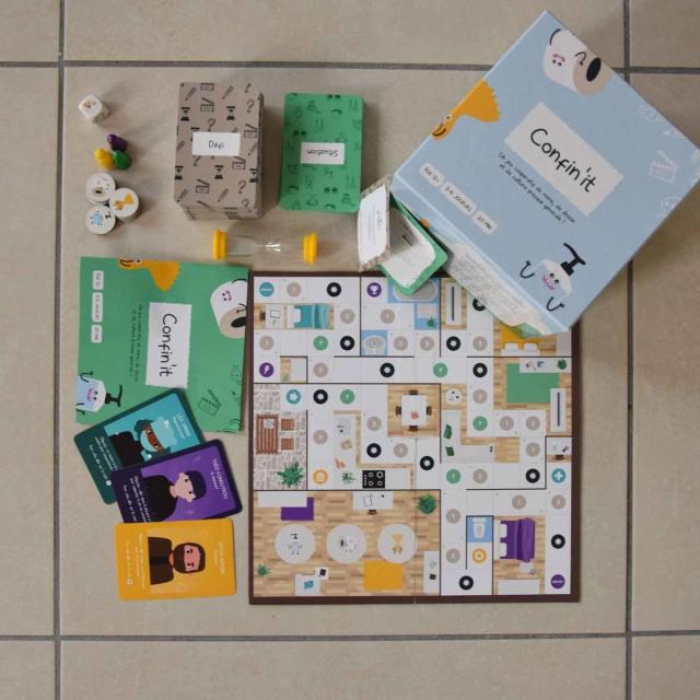 Plateau, cartes, pions et boîte du jeu Confin'it disposés sur le sol