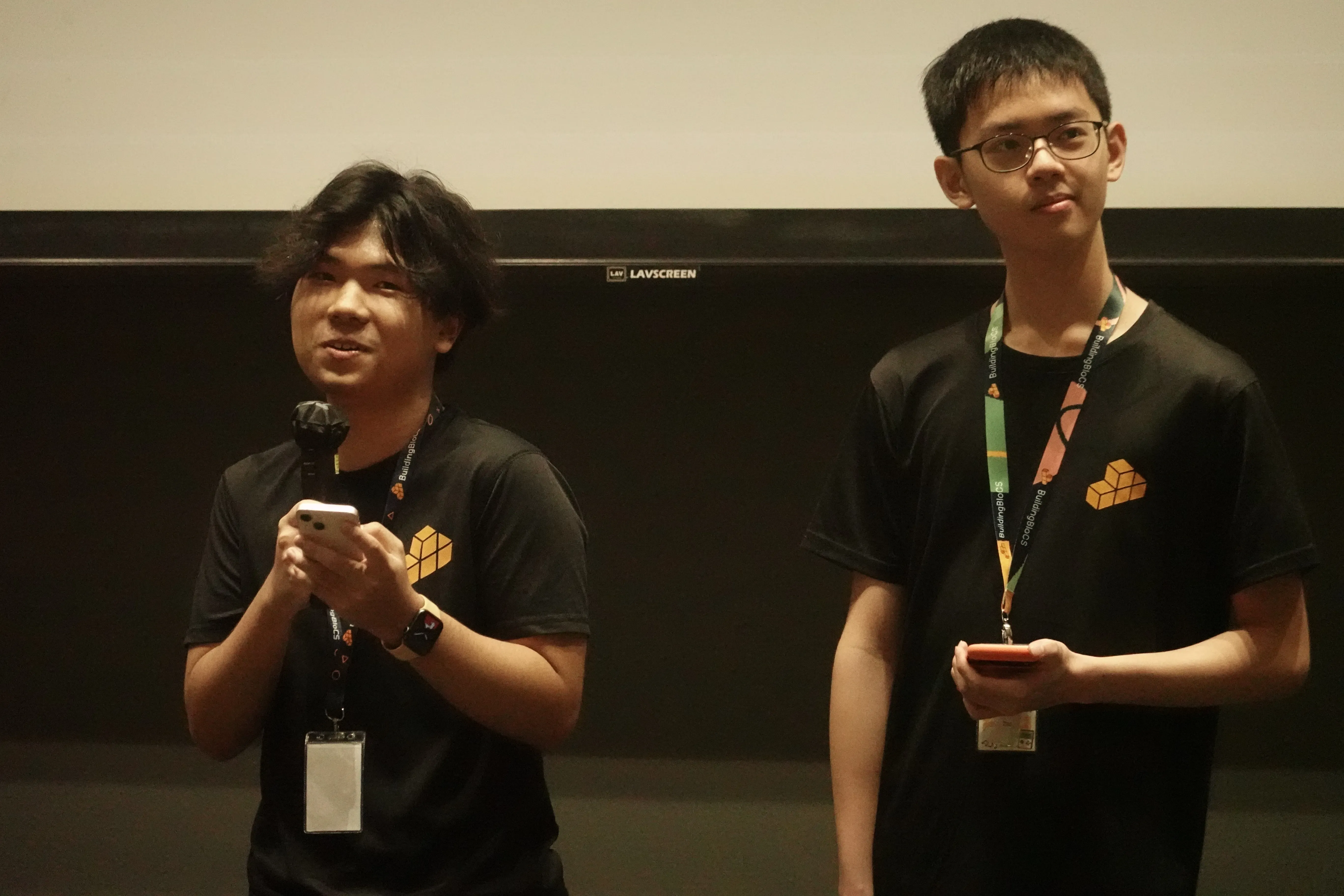 Two BuildingBloCS team members presenting on stage with microphone during event closing
