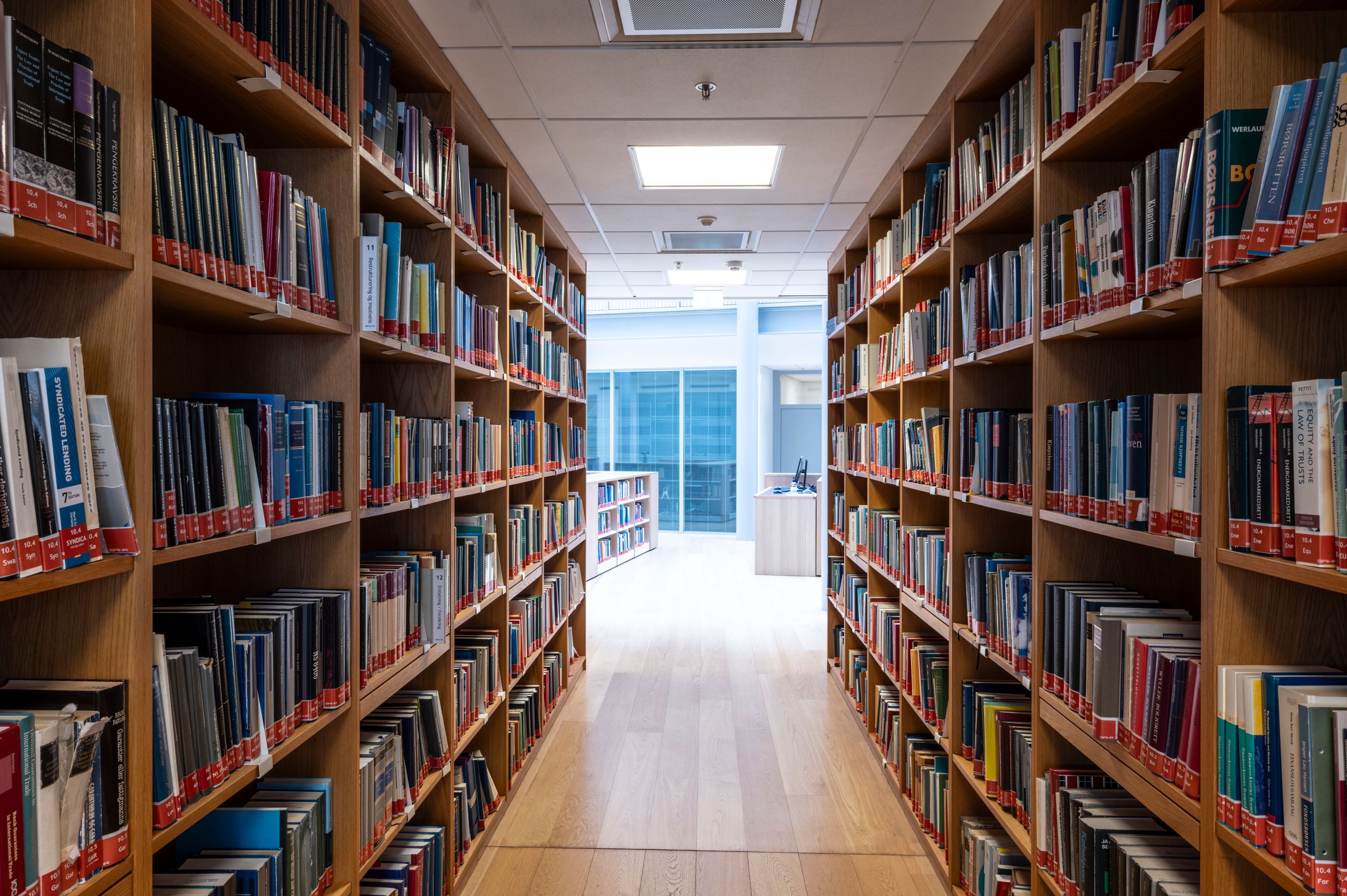 A long library aisle with wooden bookshelves full of books on both sides.