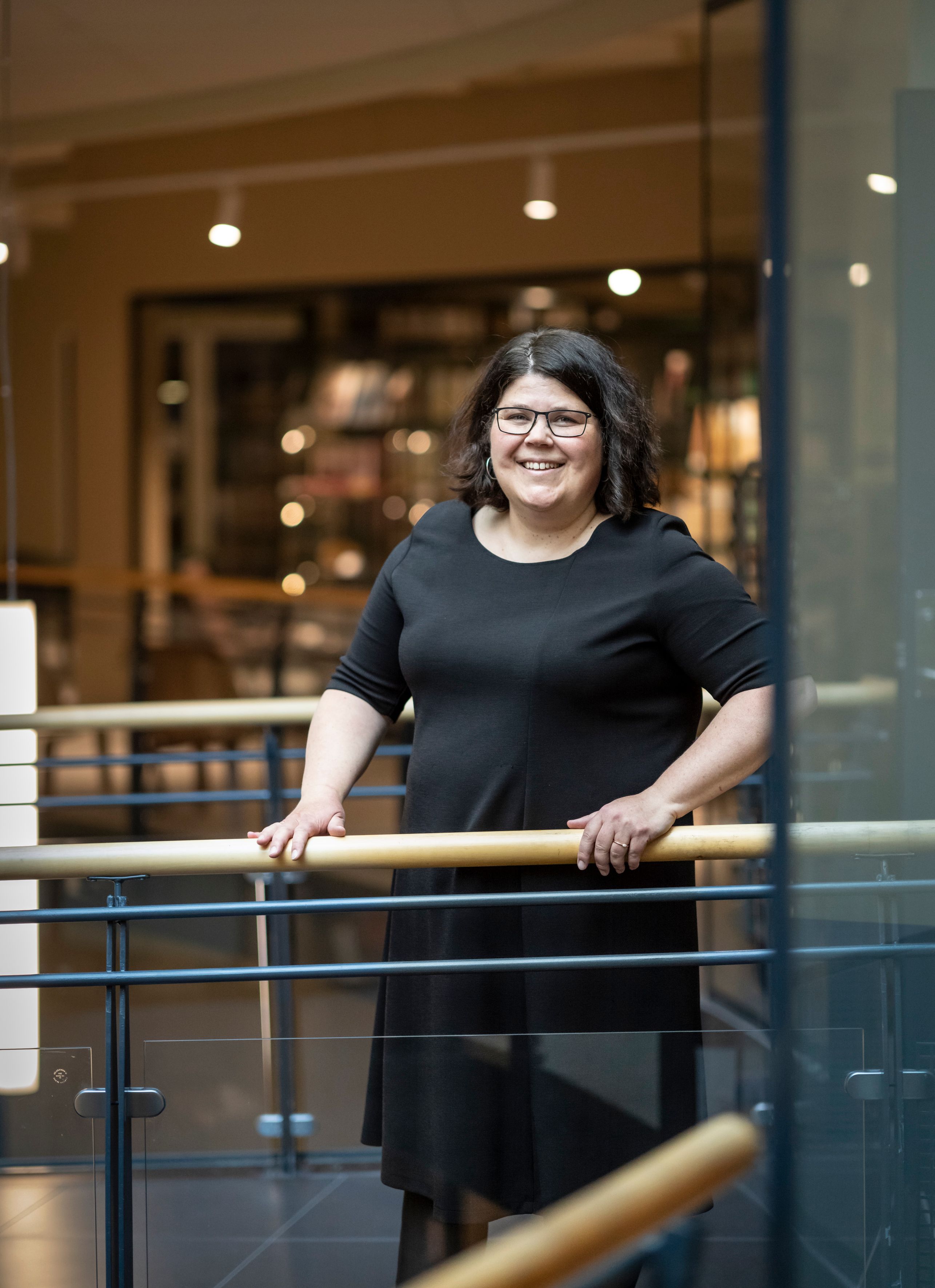 en kvinne i en svart kjole og briller lener seg på en rekkverk.