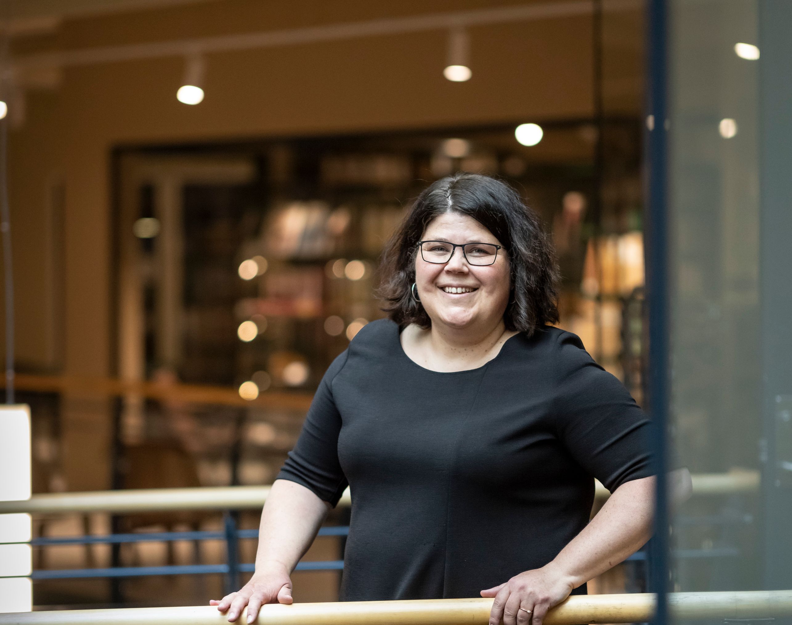 en kvinne i en svart kjole og briller lener seg på en rekkverk.