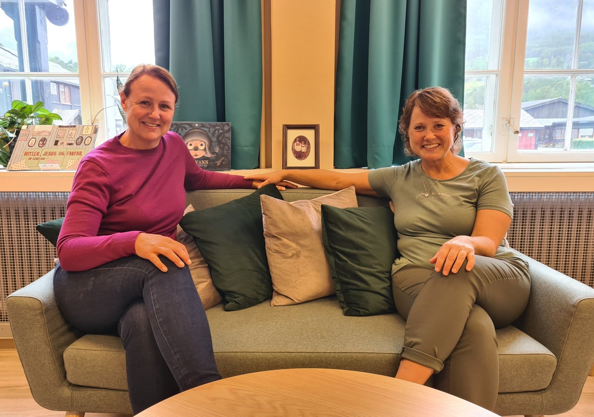 Two smiling women sit on a sofa with cushions.