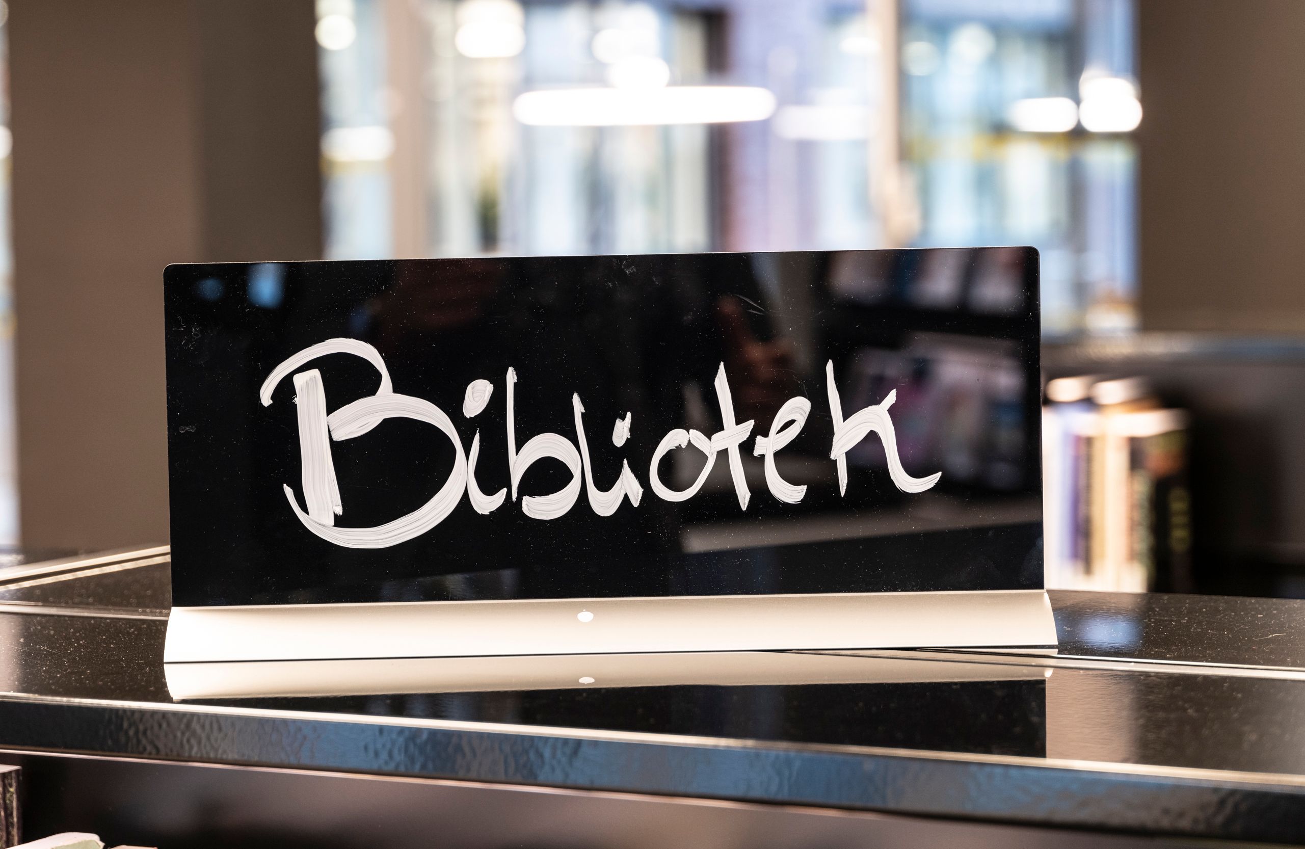 et svart skilt med ordet bibliotek skrevet på det sitter på toppen av en hylle.