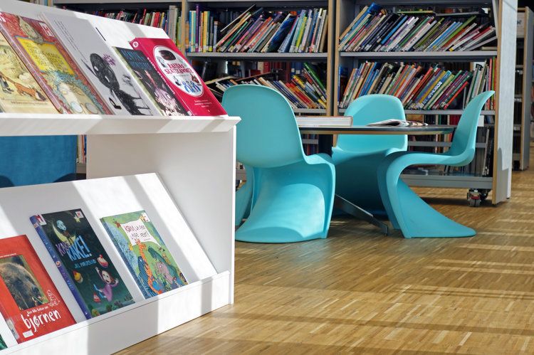 Children's books on display in a modern library with turquoise chairs and bookshelves.