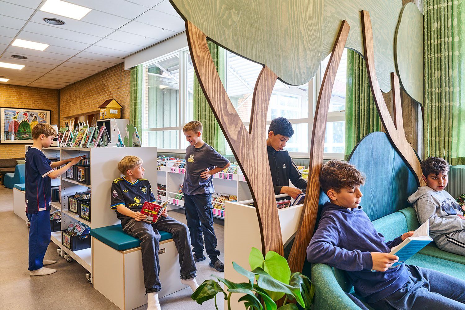 Children read and browse books in a modern library with wooden tree cutouts.