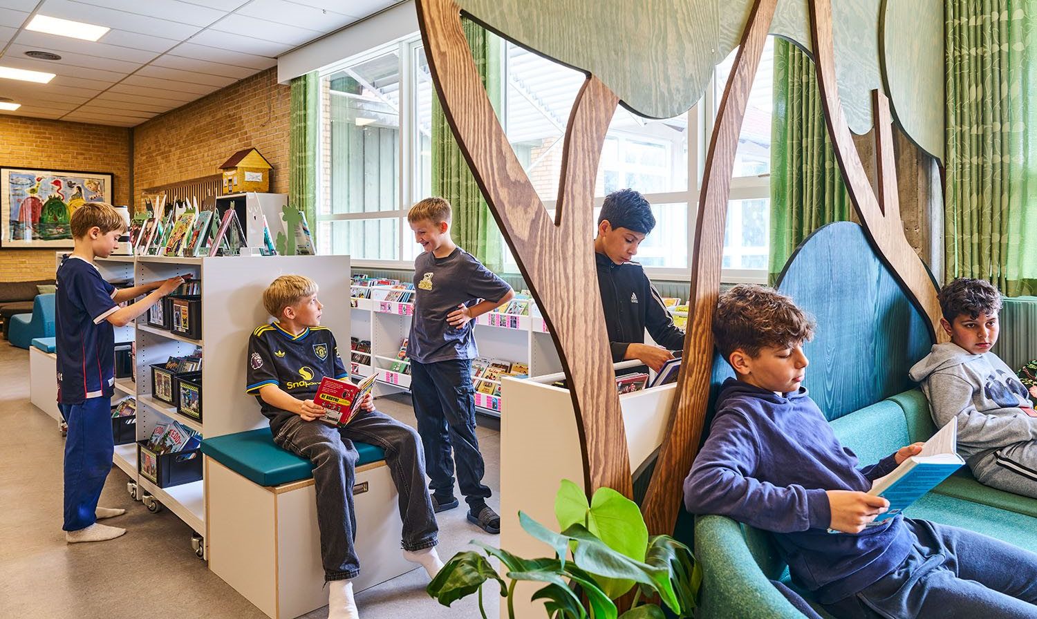 Children read and browse books in a modern library with wooden tree cutouts.
