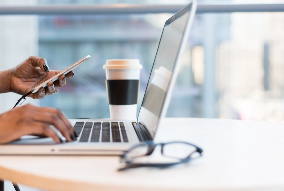 a woman is typing on a laptop while holding a cell phone
