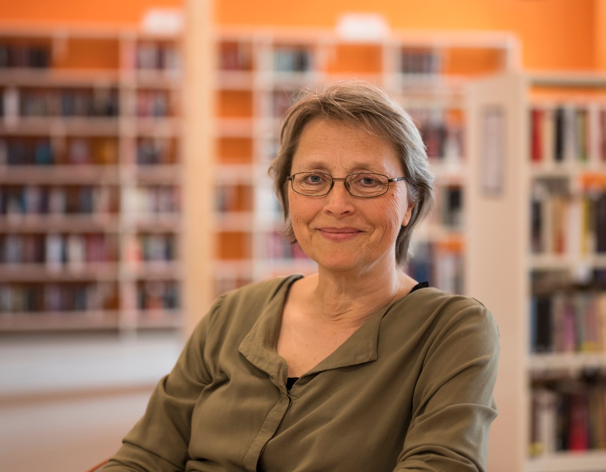 en kvinne med briller sitter ved et bord på et bibliotek
