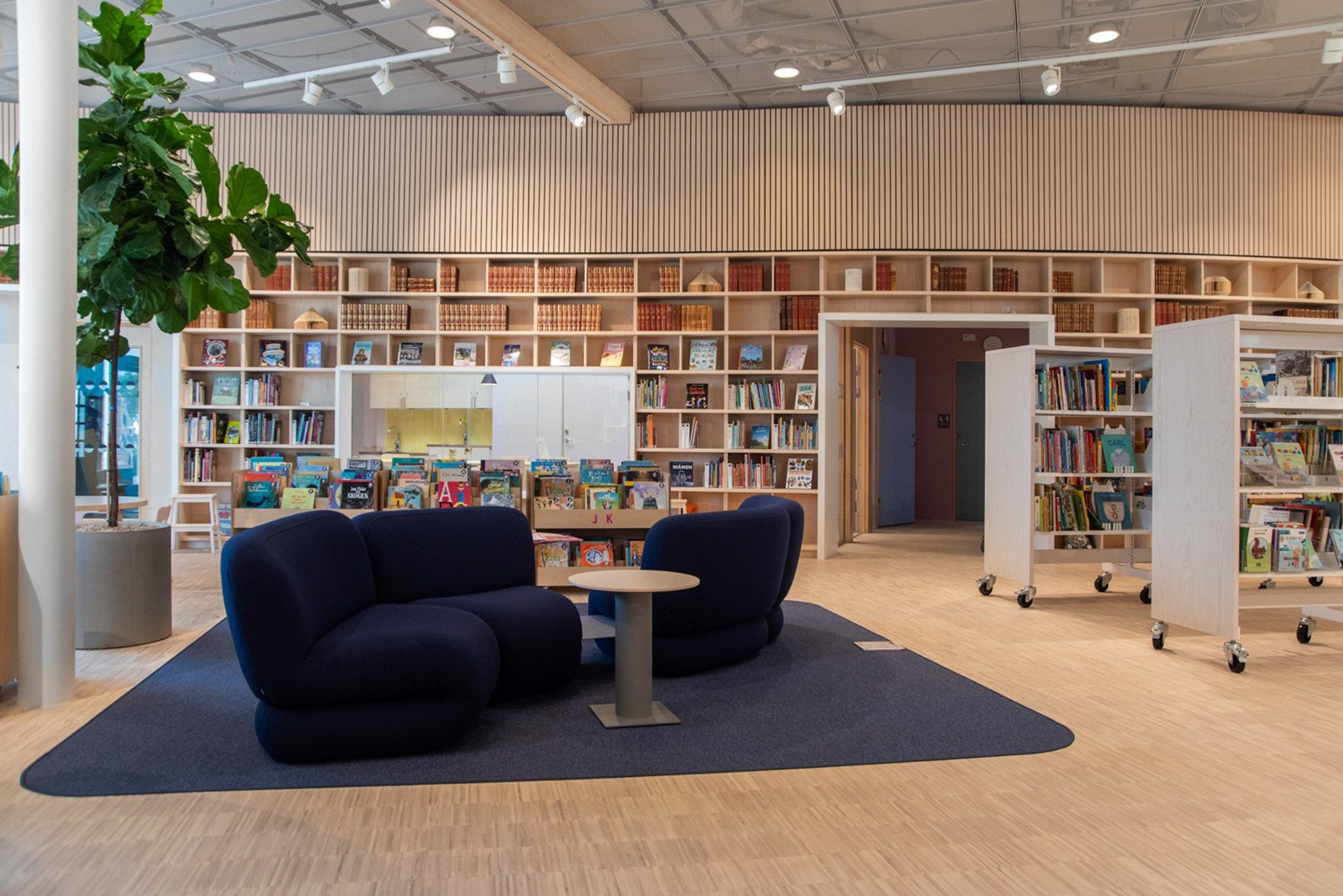 et bibliotek med mange bokreoler og en blå sittegruppe midt i rommet