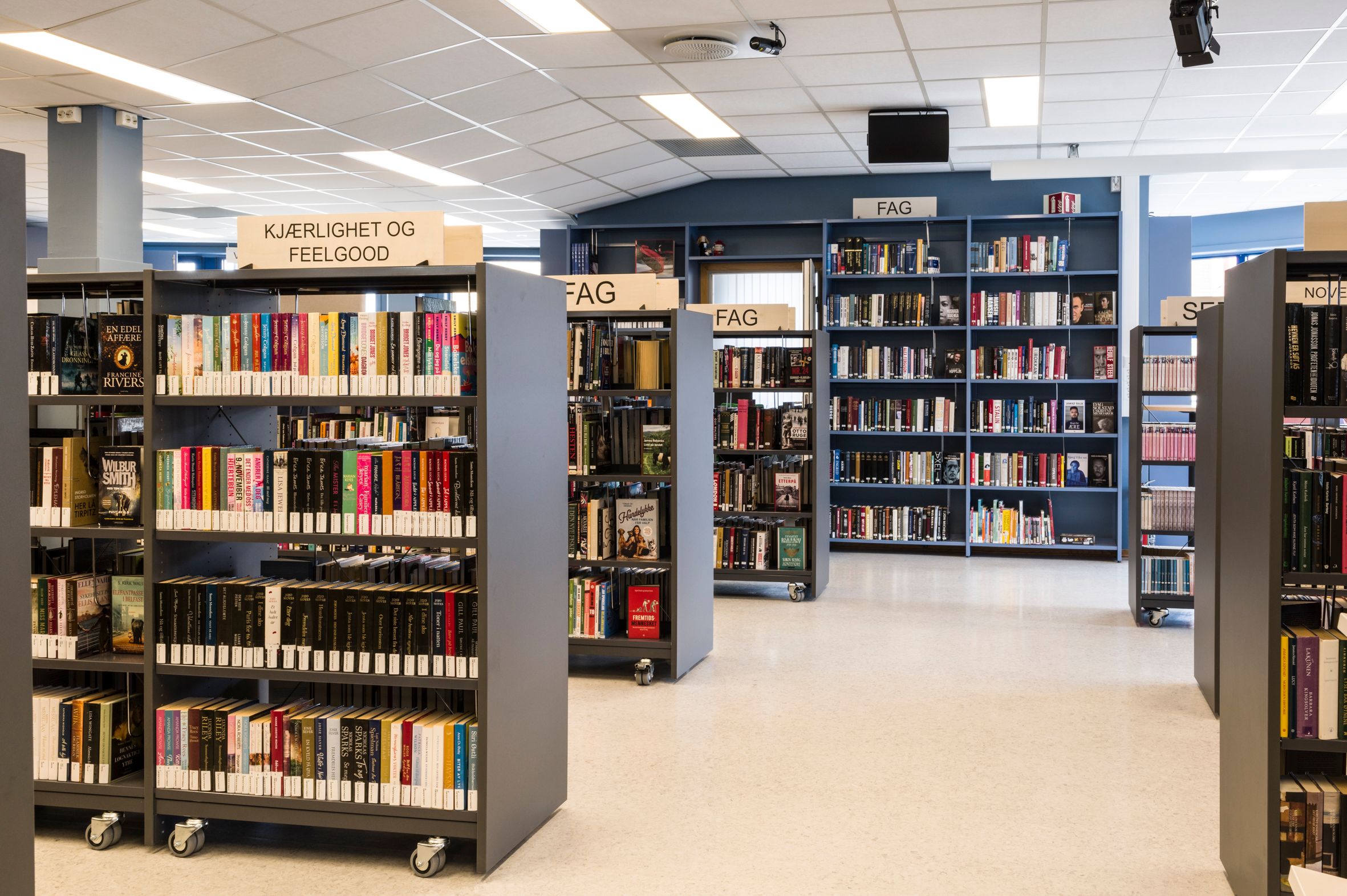 et bibliotek med lave bokreoler på hjul ute på gulvet og høye reoler langs veggen