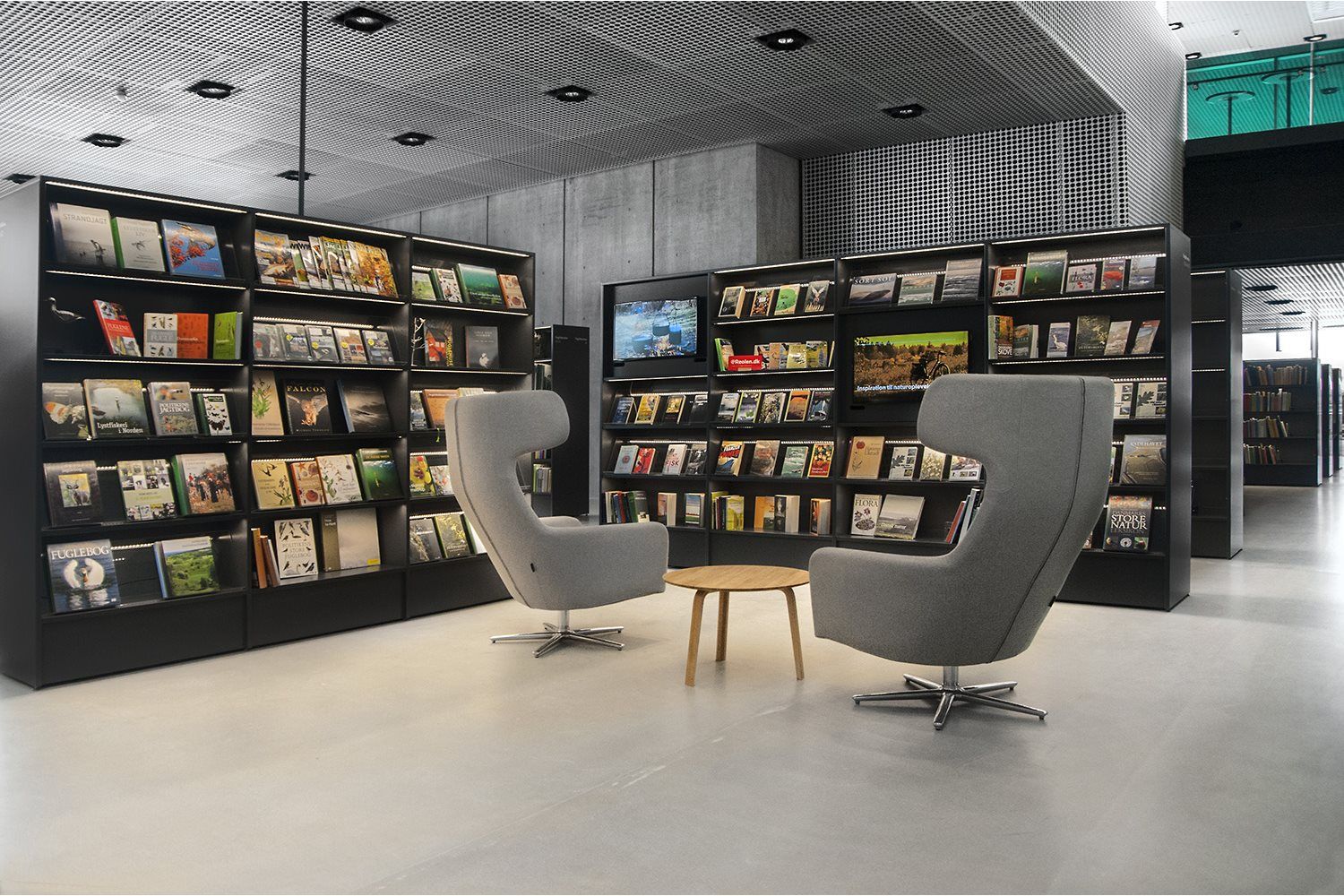 et bibliotek med lys i hver hylle med to grå lenestoler foran