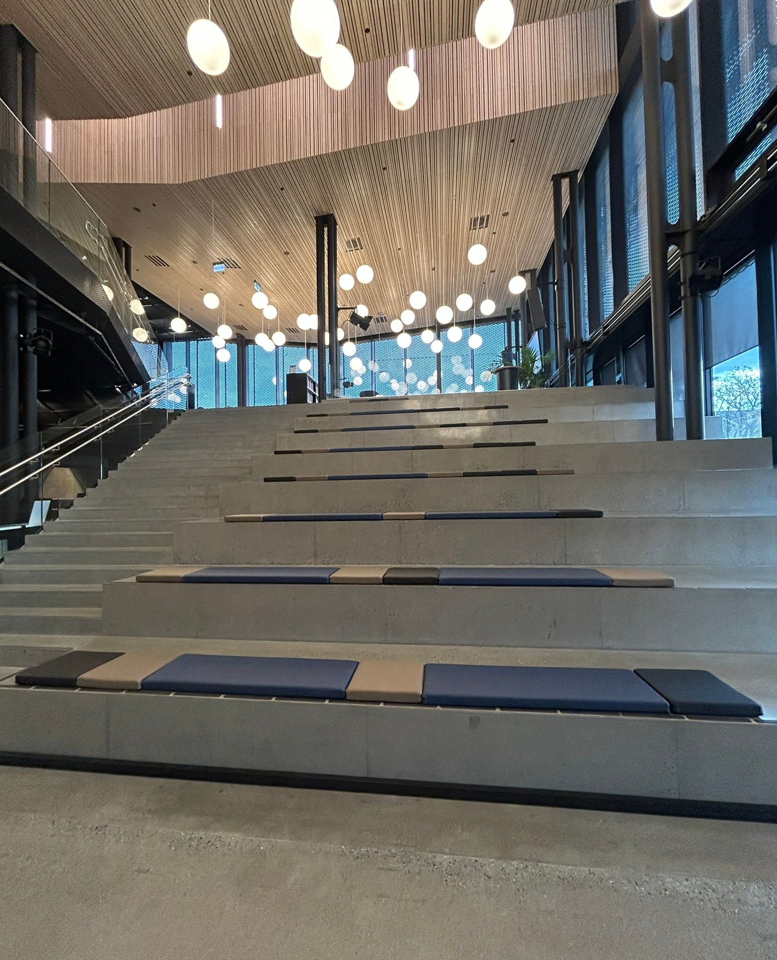 Modern hall with wide concrete stairs for seating, a wooden ceiling, and spherical pendant lights.