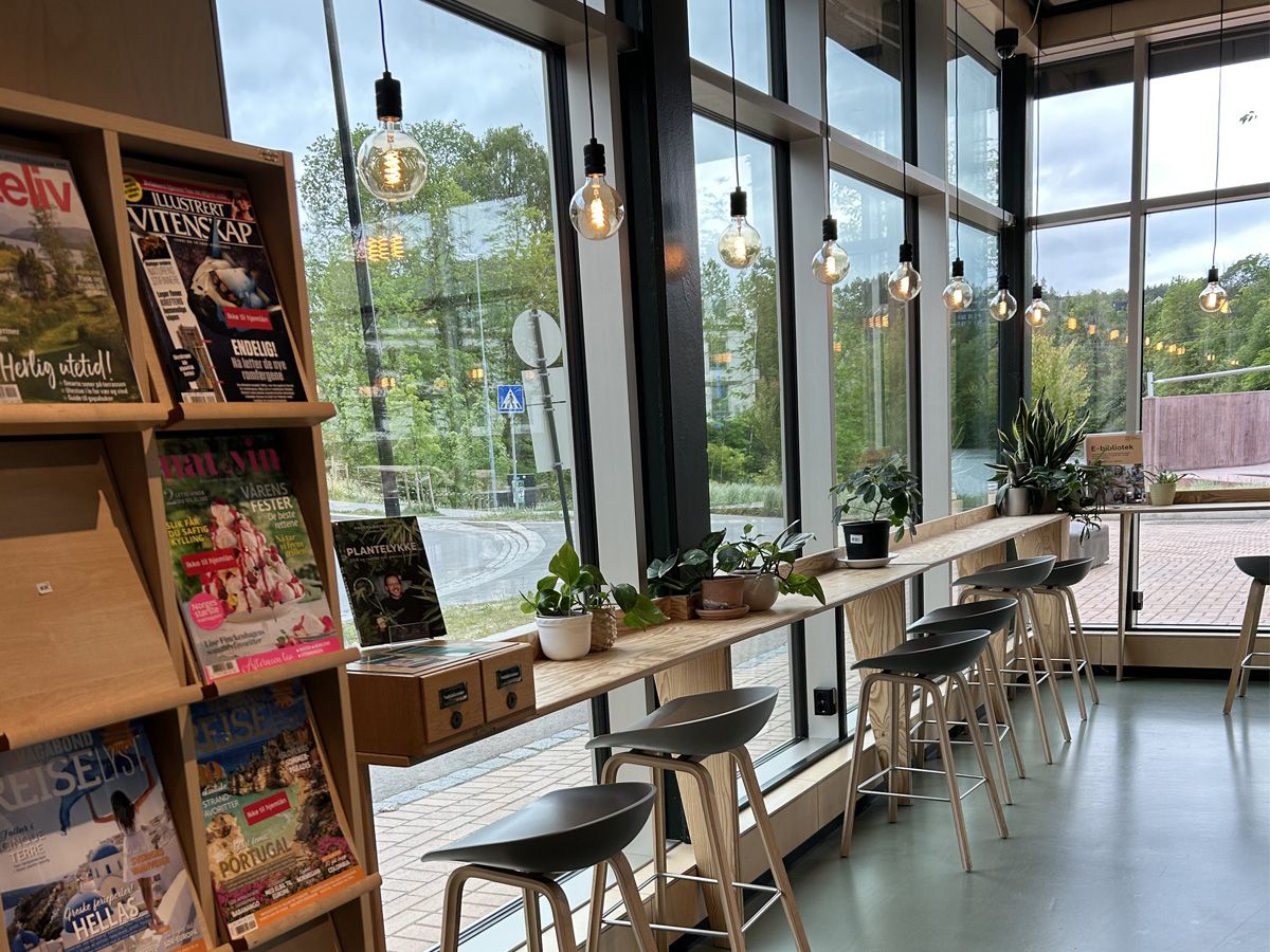 et bibliotek med et lang høybord foran store vinduer