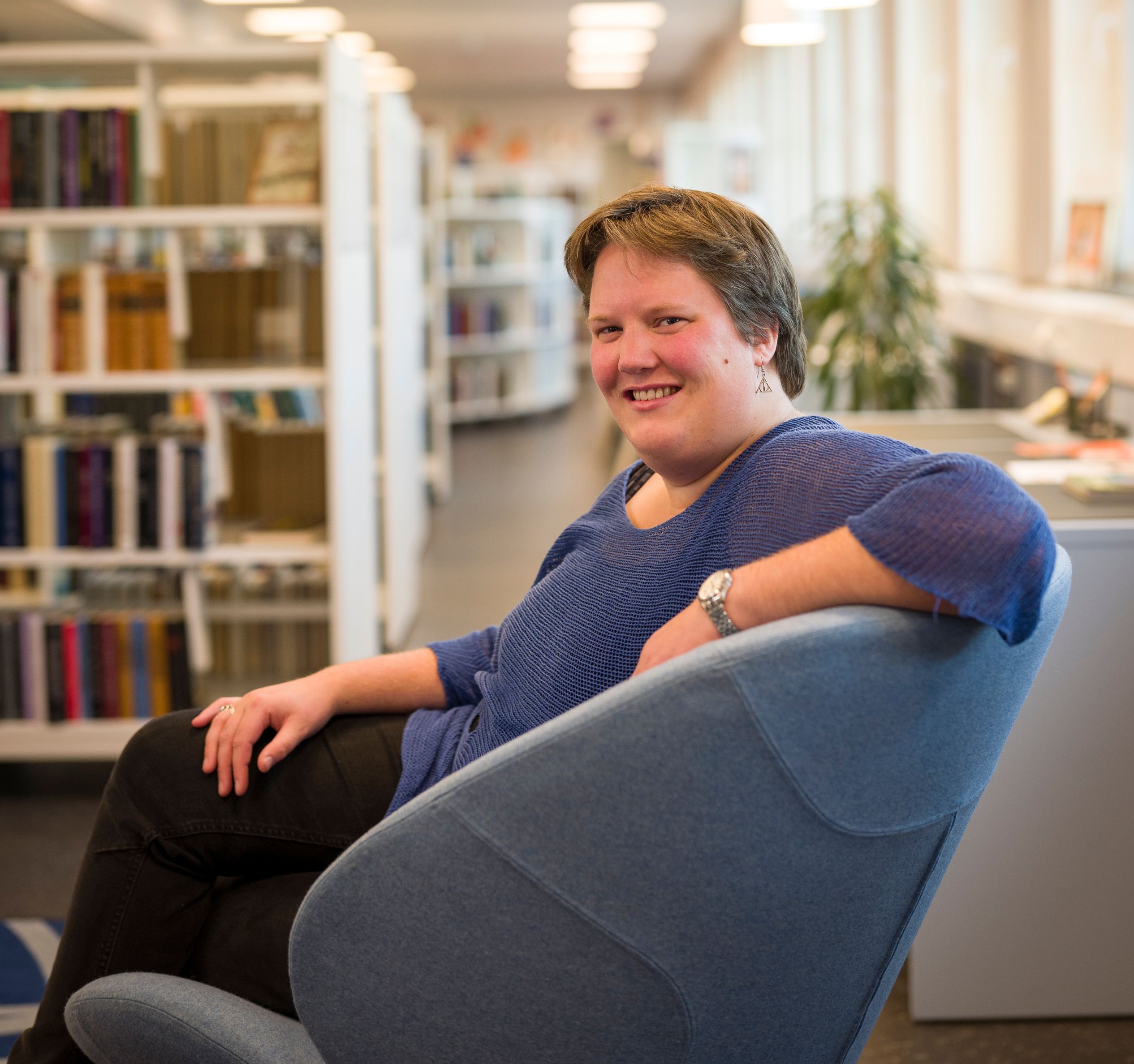 en kvinne sitter i en blå stol på et bibliotek