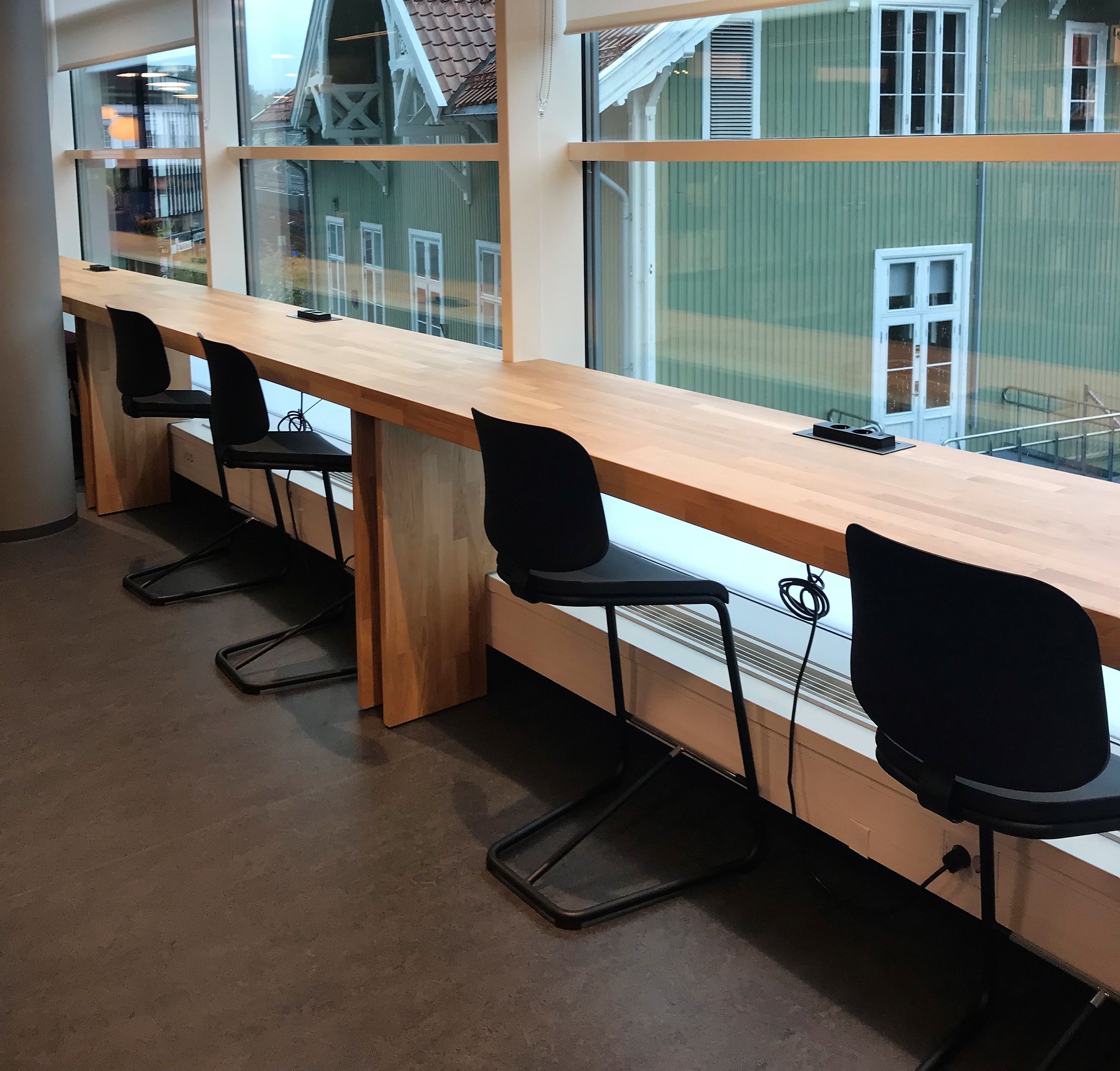 a row of desks with chairs in front of a window with a green building in the background